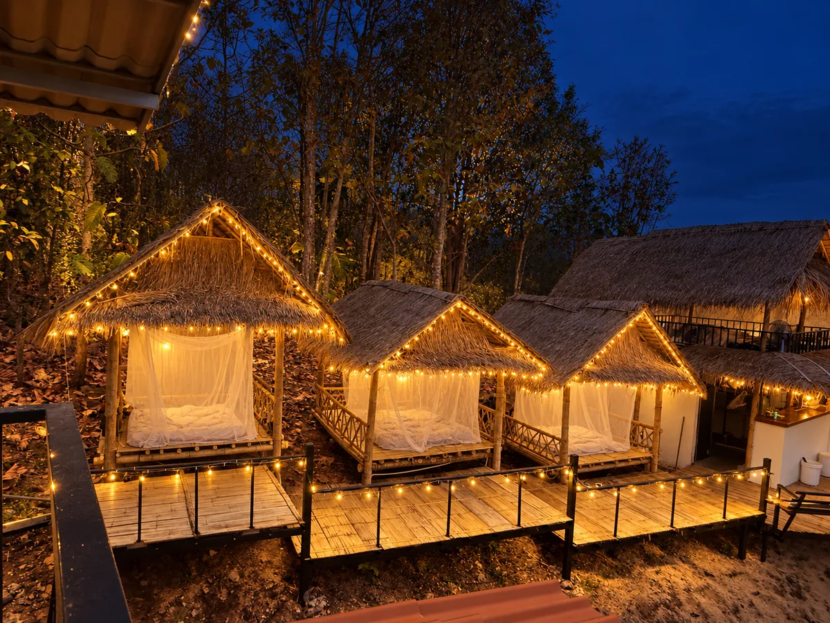 Three open-air bamboo bungalows at Bungalows & Bunks in Pai, glowing with warm string lights at night.