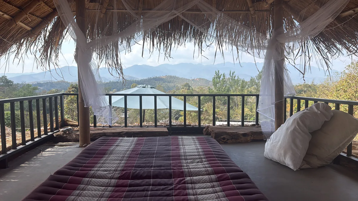 The mosquito-netted penthouse bed beneath a thatched roof at Bungalows & Bunks in Pai, looking toward the green hills.